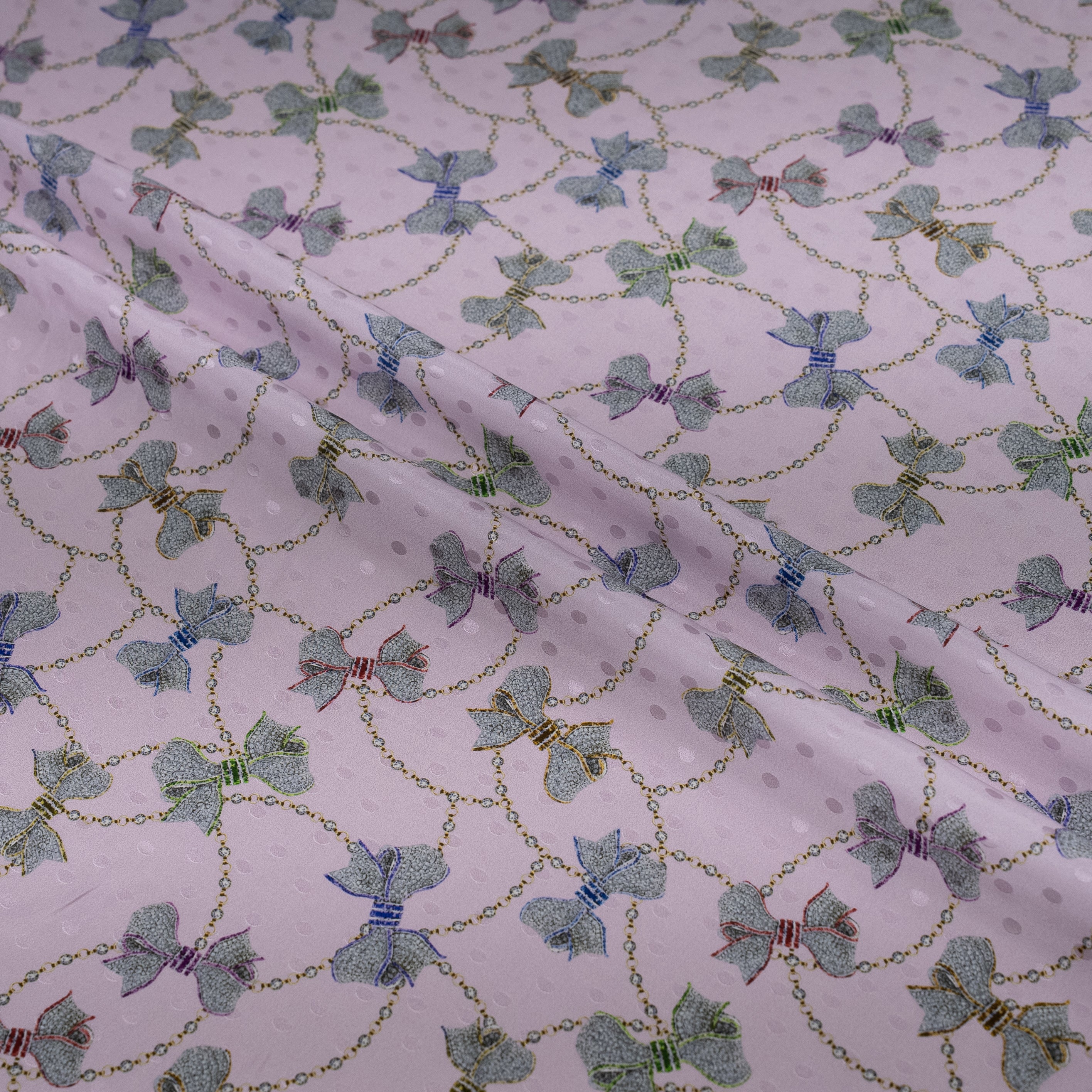 Fabric with a pattern of green bows and gold chains on a white background