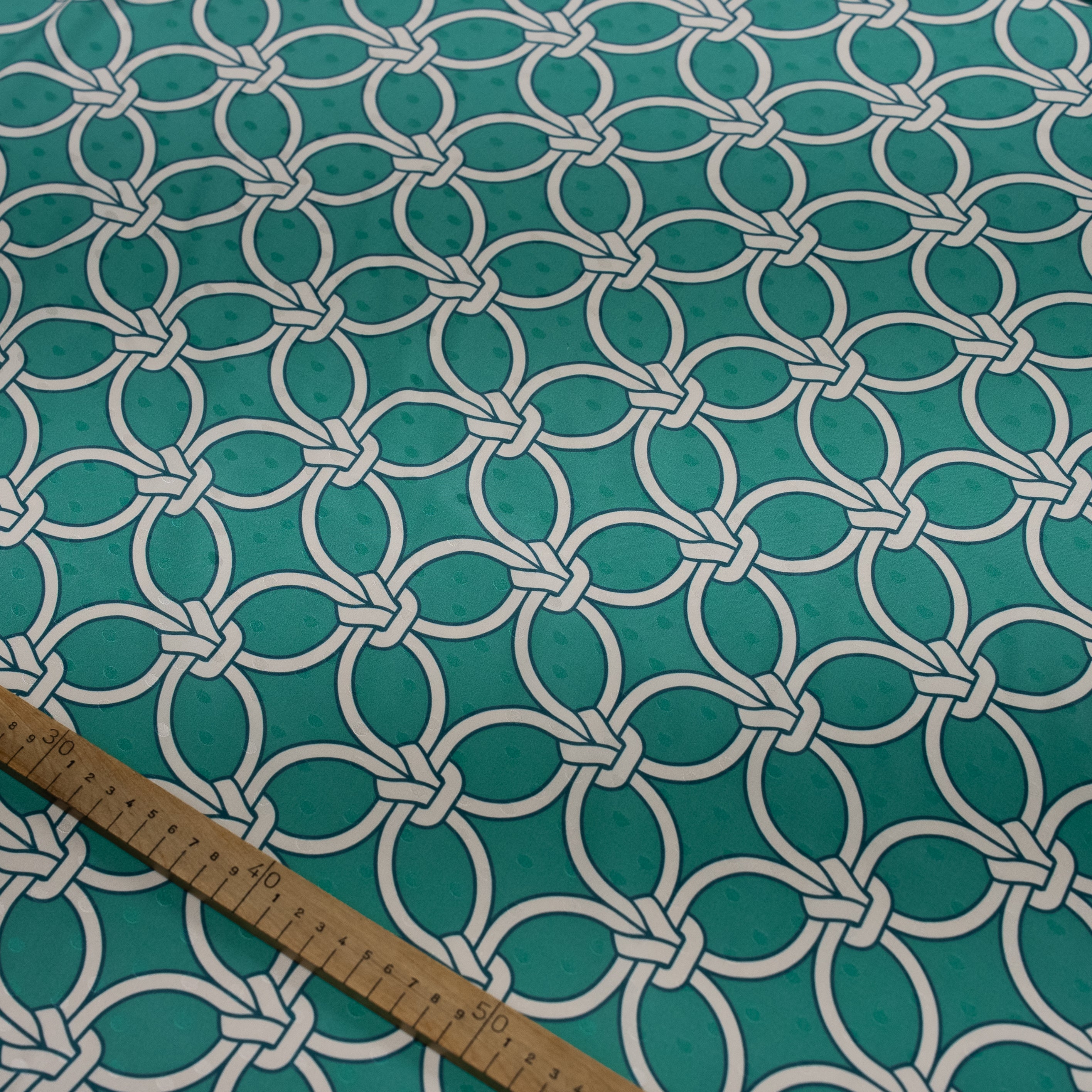 Teal fabric with white geometric pattern and wooden ruler for scale